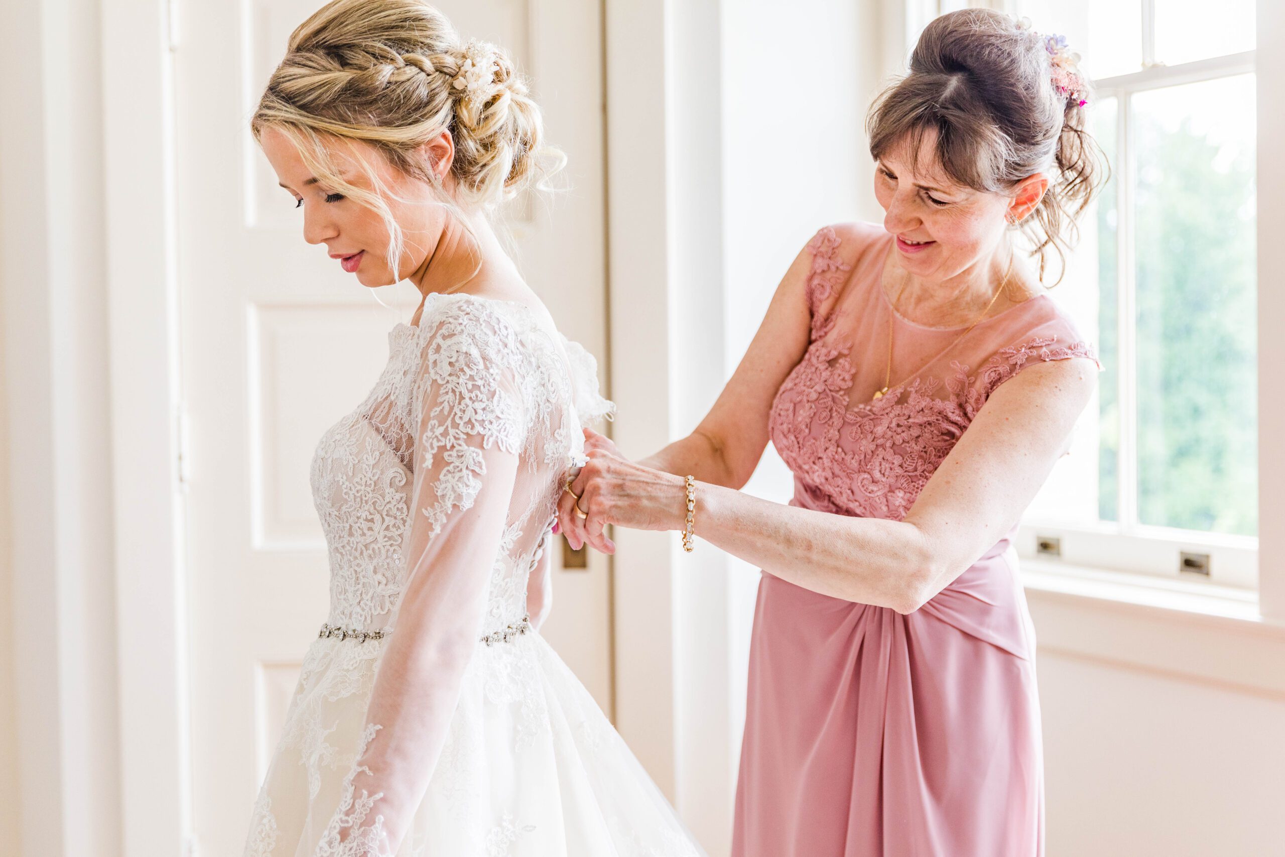 mother of the bride helping bride get dressed

