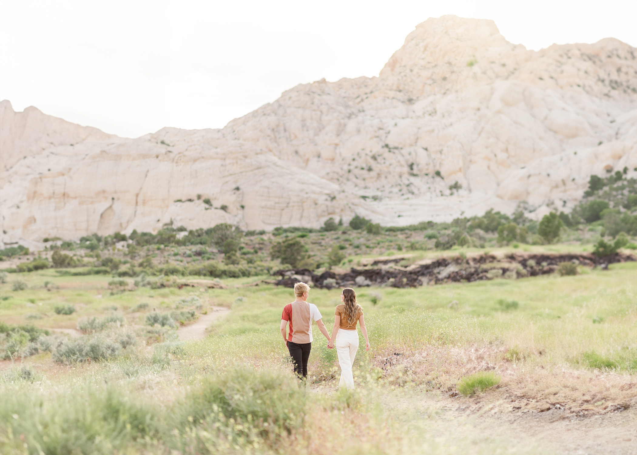couple holding hands walking through a field in Southern Utah